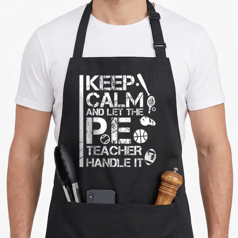 Handle teacher apron - Distressed white text and sports equipment including bat, racket, and whistle — shown on a black cotton canvas apron against a white background