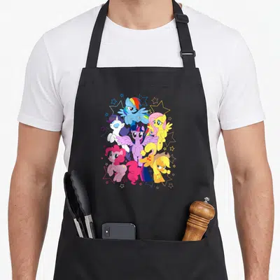 Starry magic apron - Five colorful cartoon ponies clustered with outlined stars in blue purple pink and yellow — shown on a black cotton canvas apron against a white background
