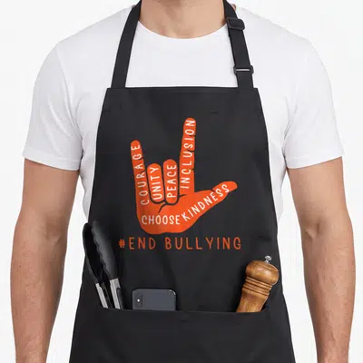 Anti unity apron - Orange hand sign language shape with white text courage unity peace inclusion choose kindness — shown on a black cotton canvas apron against a white background