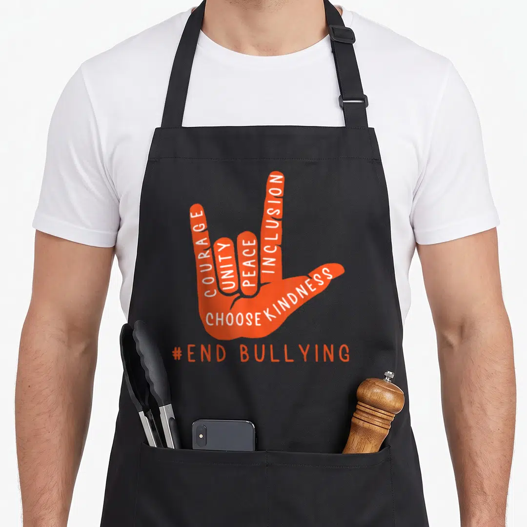 Anti unity apron - Orange hand sign language shape with white text courage unity peace inclusion choose kindness — shown on a black cotton canvas apron against a white background
