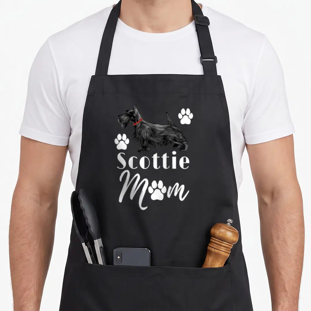 Baseball dog apron - Scottish Terrier illustration with Scottie Mom text and white paw prints — shown on a black cotton canvas apron against a white background