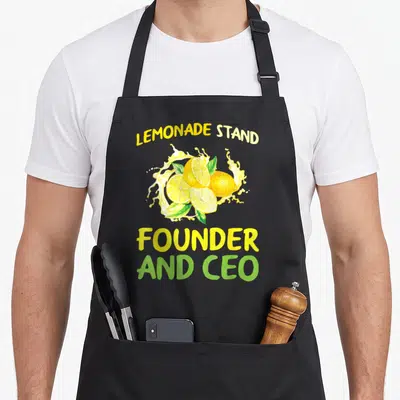 Founder lemon apron - Watercolor lemons splash with arched Lemonade Stand text and Founder And CEO below — shown on a black cotton canvas apron against a white background
