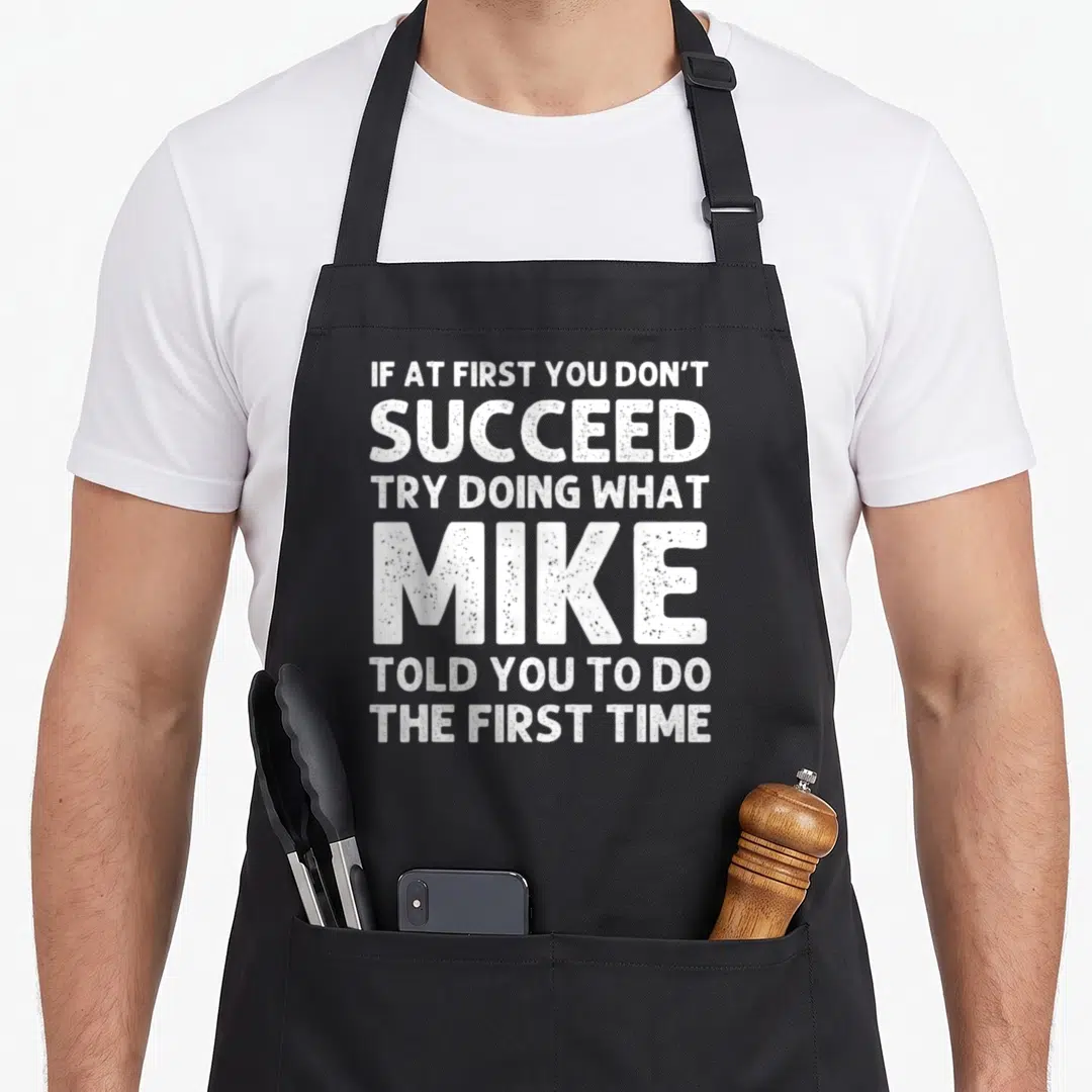 Mike christmas apron - White stacked typography reading if at first you dont succeed try doing what mike told you to do — shown on a black cotton canvas apron against a white background