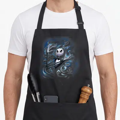 Fog jack lover apron - Jack Skellington surrounded by swirling blue and grey smoke with movie title text — shown on a black cotton canvas apron against a white background
