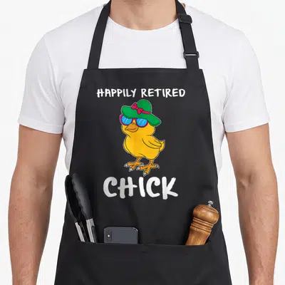 Chick funny retirement aprons - Cartoon yellow chick wearing green hat and sunglasses with happily retired chick text — shown on a black cotton canvas apron against a white background