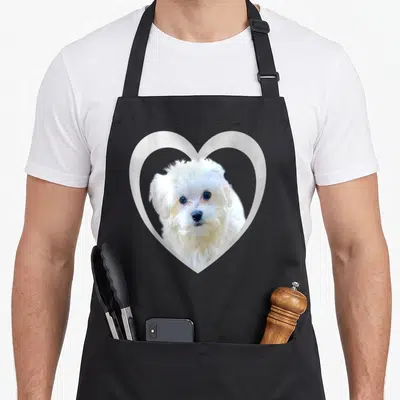 Cute maltese dog apron - Photo of white dog face inside white heart outline — shown on a black cotton canvas apron against a white background