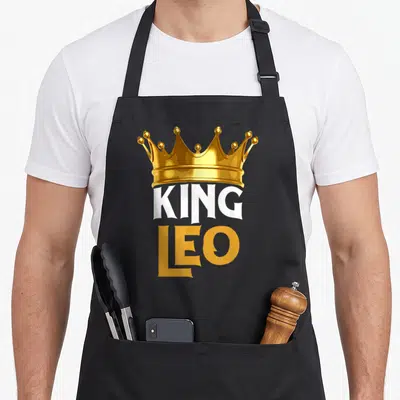 Leo chef outfit with apron - Gold crown above white KING and gold LEO text — shown on a black cotton canvas apron against a white background