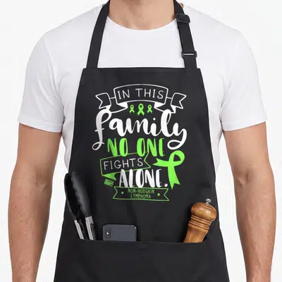 Awareness family aprons - White and lime green typography reading IN THIS family NO ONE FIGHTS ALONE with ribbons — shown on a black cotton canvas apron against a white background