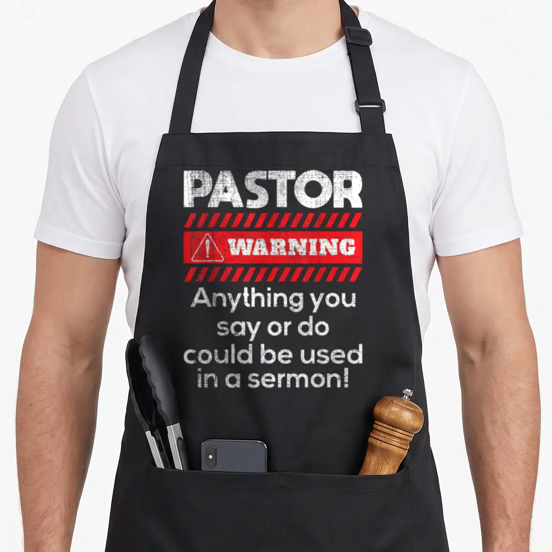 Anything minister apron - Distressed white and red warning sign text reading Pastor Warning Anything You Say Or Do — shown on a black cotton canvas apron against a white background