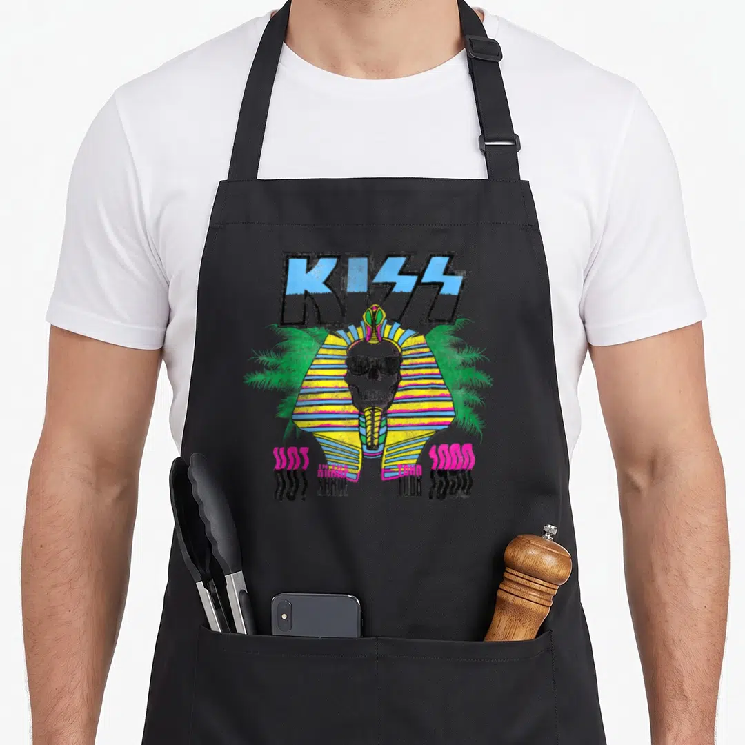 Kiss zapiekanka apron - Retro skull with nemes headcloth and 1980 tour text surrounded by palm trees — shown on a black cotton canvas apron against a white background