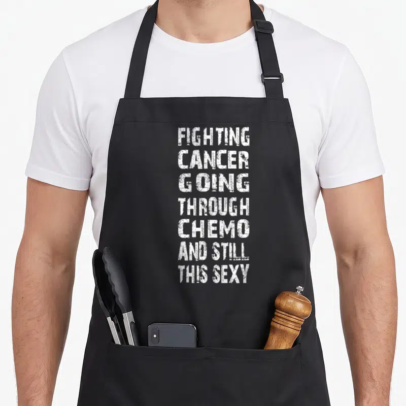 Cancer sledding apron - White stacked text reading Fighting Cancer Going Through Chemo And Still This Sexy — shown on a black cotton canvas apron against a white background
