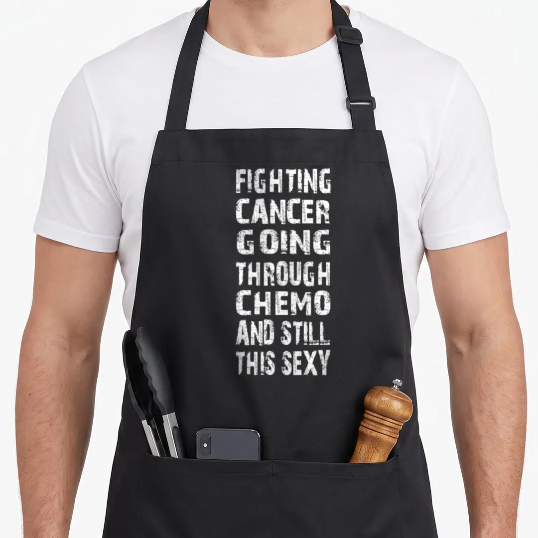 Cancer sledding apron - White stacked text reading Fighting Cancer Going Through Chemo And Still This Sexy — shown on a black cotton canvas apron against a white background