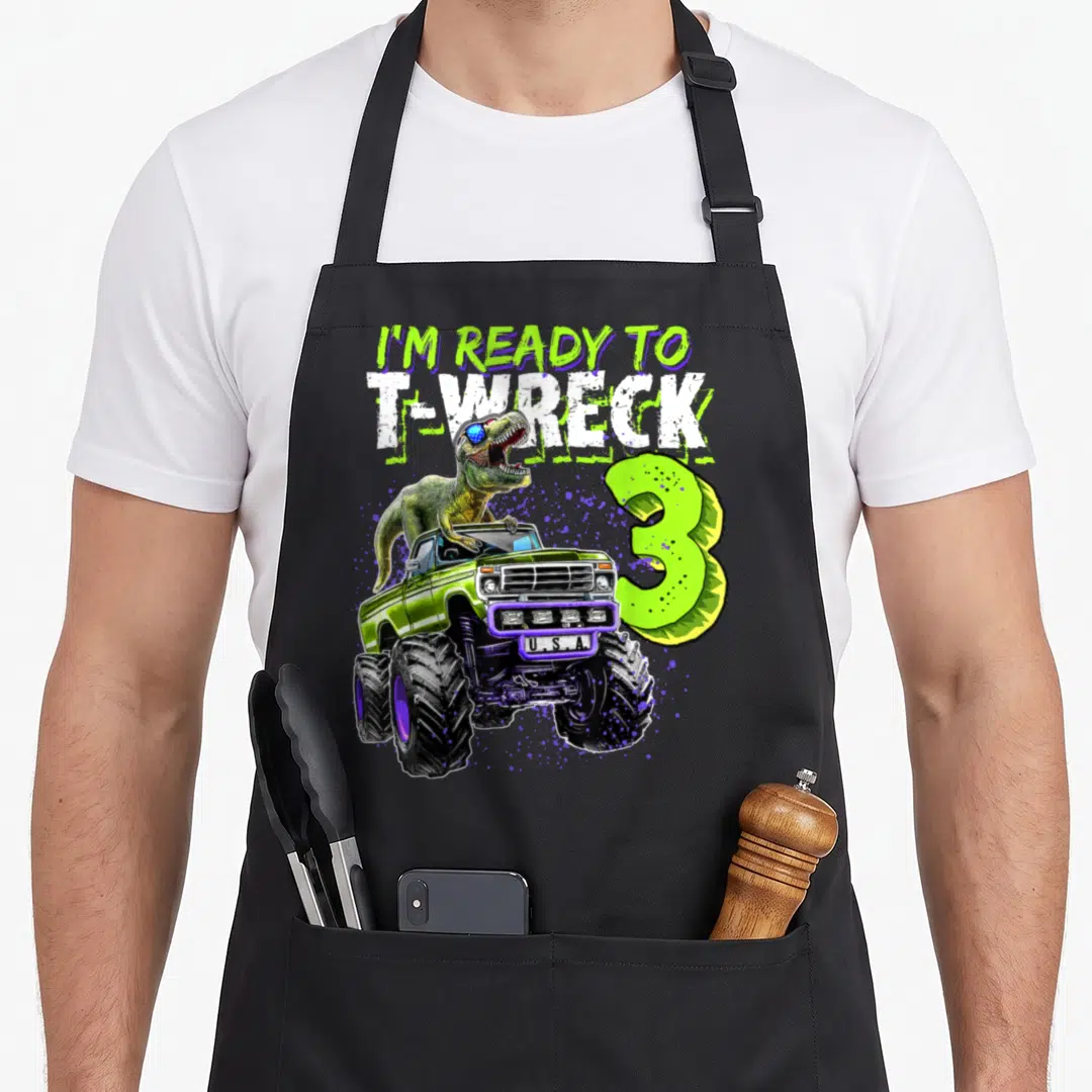 Ready wreck truck apron - T-Rex in lime green monster truck with purple splatters and text reading I'm ready to T-wreck — shown on a black cotton canvas apron against a white background