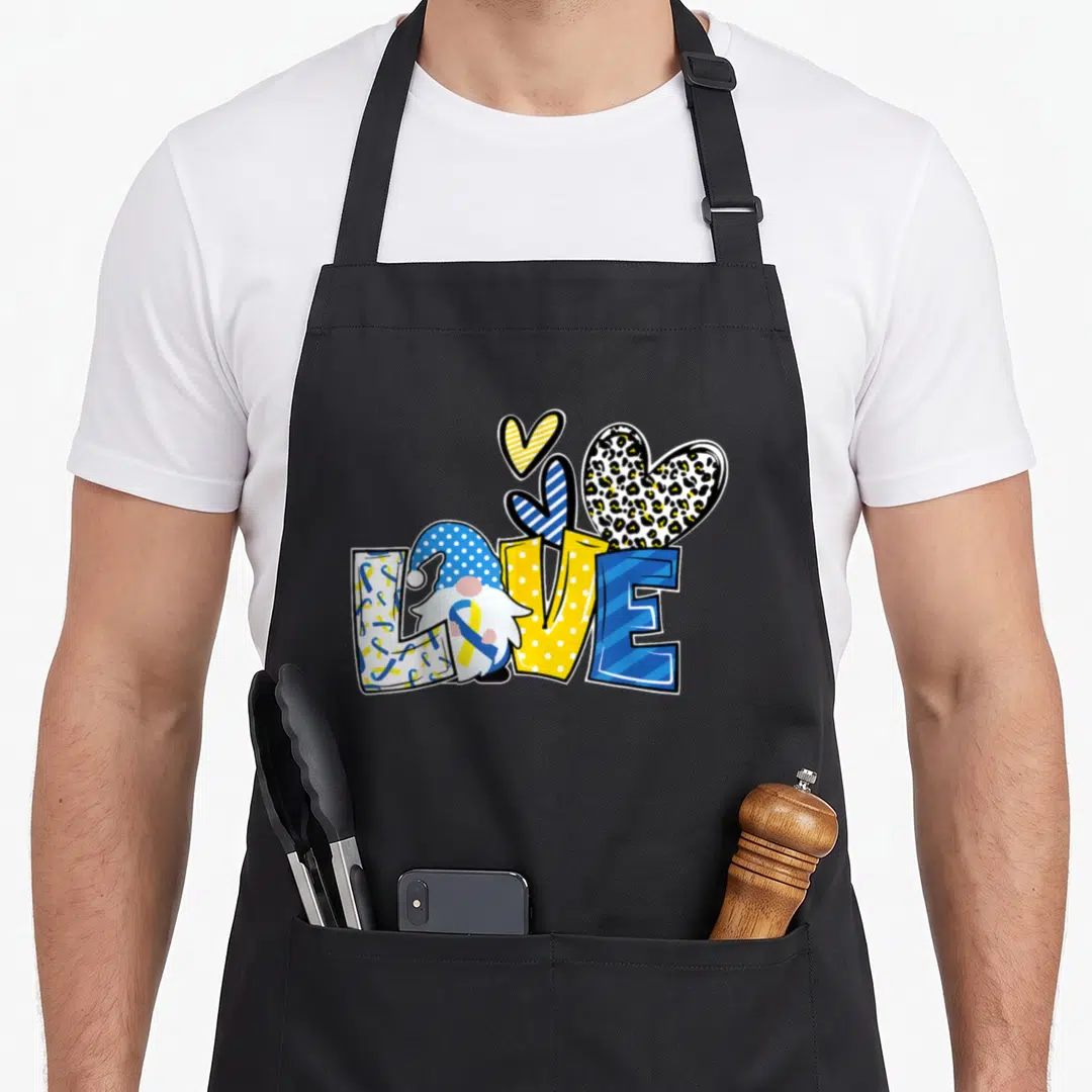 Syndrome ribbon apron - LOVE text with integrated gnome and three patterned hearts in blue yellow and white — shown on a black cotton canvas apron against a white background