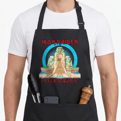 Powerslave collection apron - Pharaoh statue between two sphinxes with IRON MAIDEN POWERSLAVE text in red and gold — shown on a black cotton canvas apron against a white background