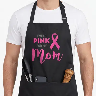 Funny breast cancer awareness aprons - I WEAR PINK FOR MY Mom text with pink ribbon on grey background — shown on a black cotton canvas apron against a white background