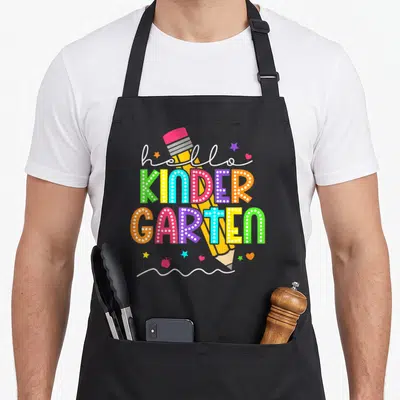 Kinder school kindergarten teacher apron - Hello KINDER GARTEN text behind yellow pencil with colorful stars and hearts — shown on a black cotton canvas apron against a white background
