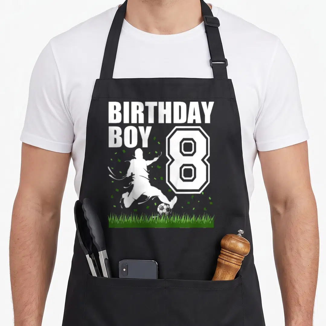 Theme 8th birthday apron - Soccer player silhouette kicking ball next to large number 8 and confetti on grass — shown on a black cotton canvas apron against a white background