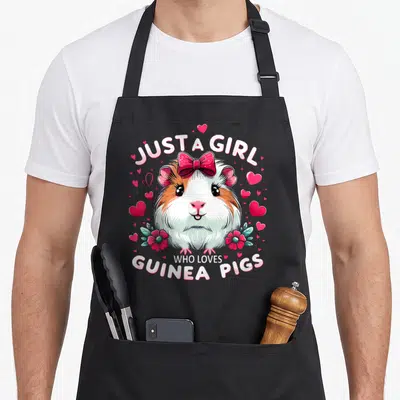 Funny pig guinea mom apron - Cartoon guinea pig with red bow and pink hearts under text JUST A GIRL WHO LOVES GUINEA — shown on a black cotton canvas apron against a white background