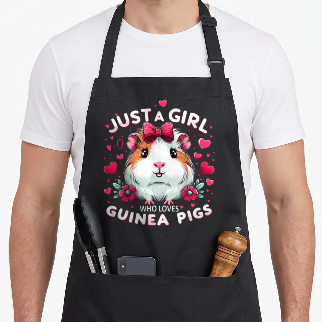Funny pig guinea mom apron - Cartoon guinea pig with red bow and pink hearts under text JUST A GIRL WHO LOVES GUINEA — shown on a black cotton canvas apron against a white background