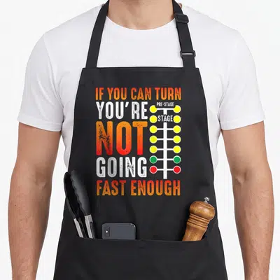 Dragster car apron - IF YOU CAN TURN typography next to a multi-colored drag racing light tree — shown on a black cotton canvas apron against a white background