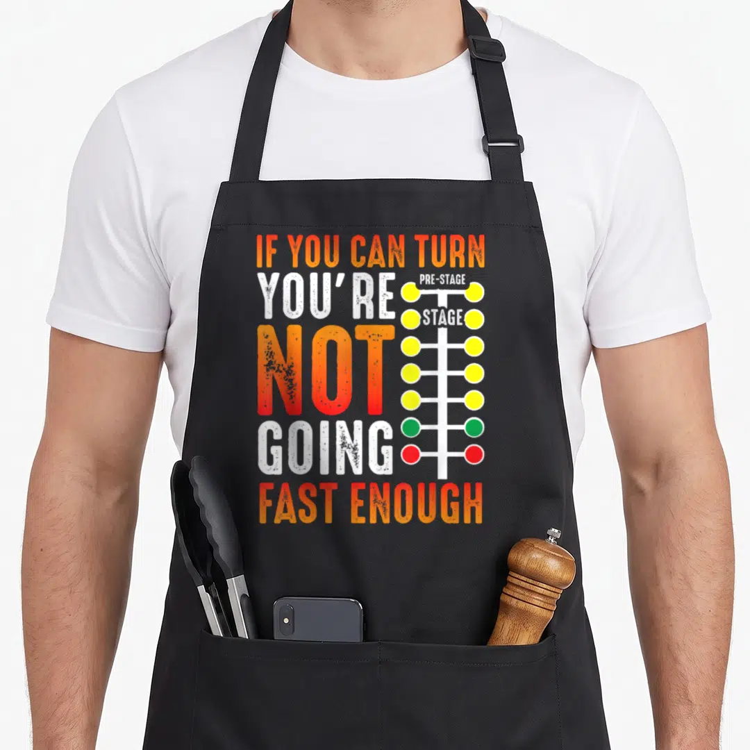 Dragster car apron - IF YOU CAN TURN typography next to a multi-colored drag racing light tree — shown on a black cotton canvas apron against a white background