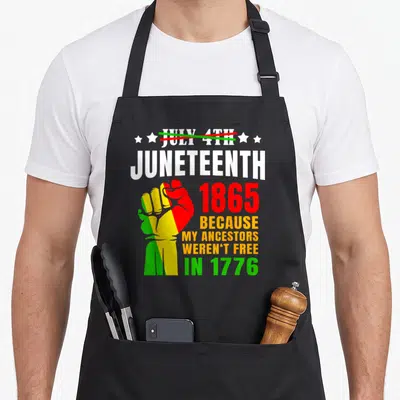 June african american aprons - Raised fist in red yellow and green with text about ancestors not being free in 1776 — shown on a black cotton canvas apron against a white background