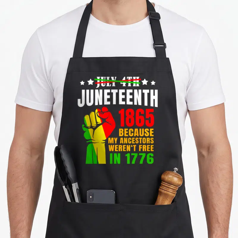 June african american aprons - Raised fist in red yellow and green with text about ancestors not being free in 1776 — shown on a black cotton canvas apron against a white background