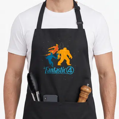 Studio fantastic first steps apron - Four colorful superhero silhouettes andFantastic 4text logo — shown on a black cotton canvas apron against a white background