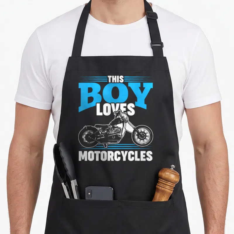 Motor bike apron - THIS BOY LOVES MOTORCYCLES text with white bike and blue lines — shown on a black cotton canvas apron against a white background