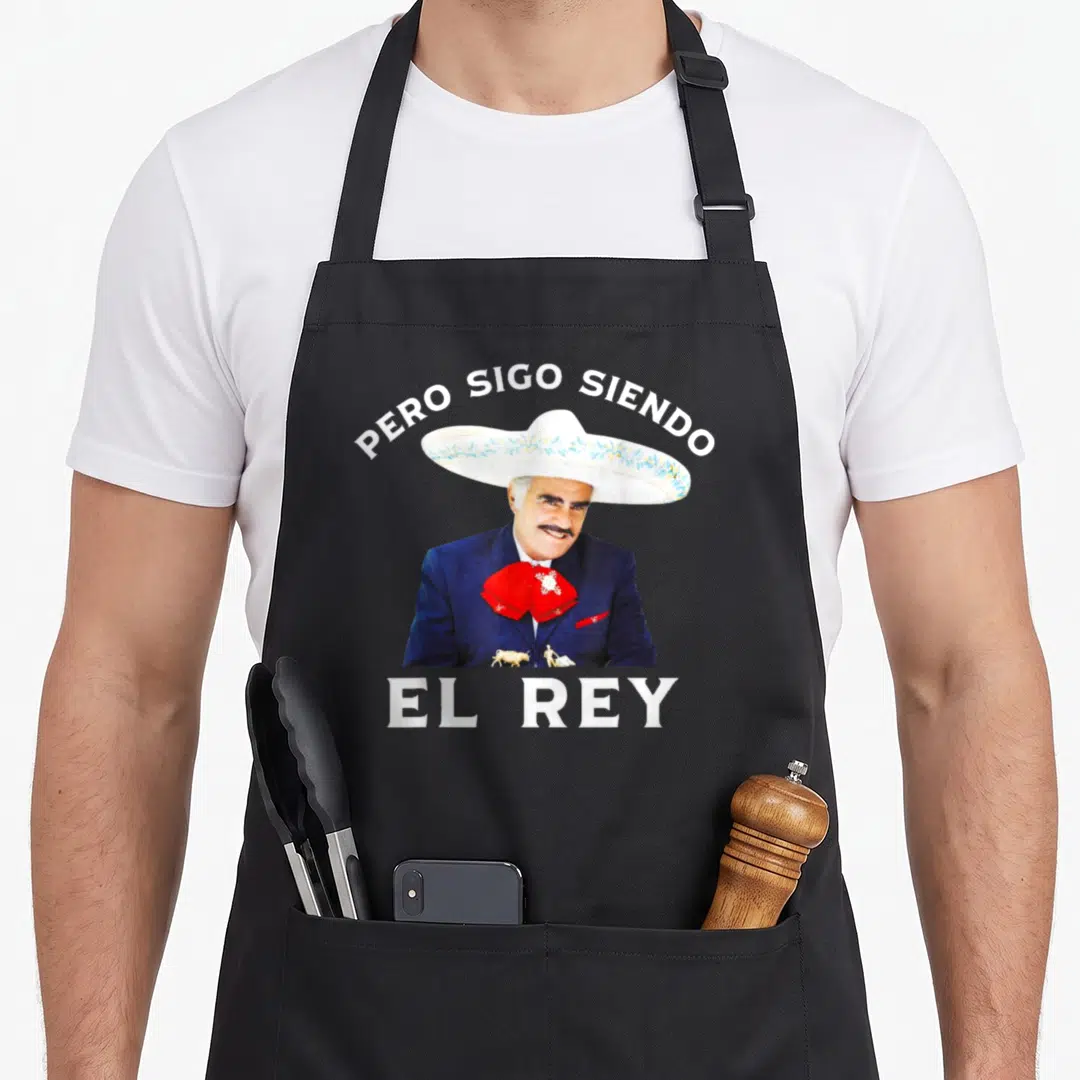 Chente mexico apron - Man in sombrero with Pero Sigo Siendo El Rey text and bullfighting scene on chest — shown on a black cotton canvas apron against a white background