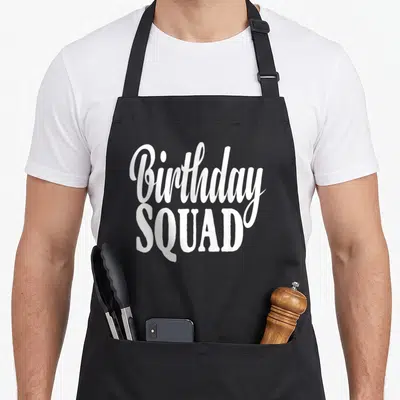 Funny squad birthday apron - White stacked text reading Birthday SQUAD in mixed fonts on grey background — shown on a black cotton canvas apron against a white background