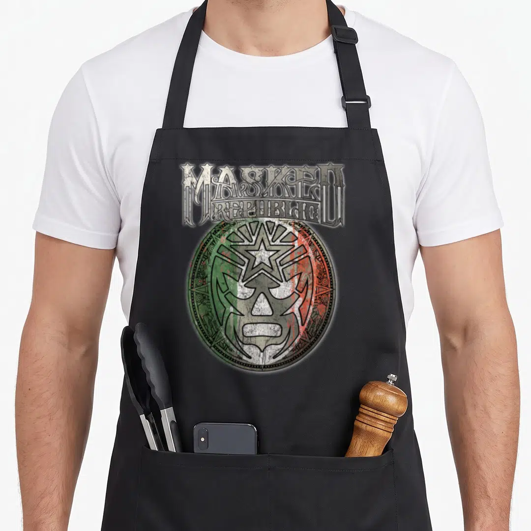 Masked lucha libre apron - Distressed MASKED REPUBLIC text above a green white and red lucha libre mask emblem — shown on a black cotton canvas apron against a white background