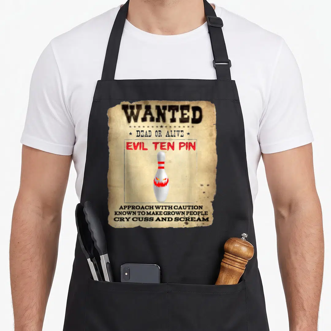 Evil pins for aprons - Wanted poster with monster faced bowling pin and red text on beige paper — shown on a black cotton canvas apron against a white background