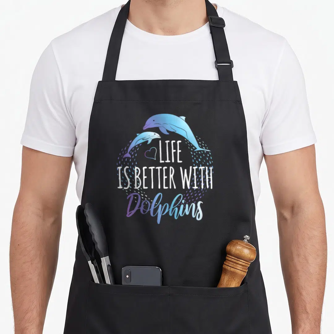 Better dolphin apron - Two blue and purple dolphins arching over a heart and text surrounded by water droplets — shown on a black cotton canvas apron against a white background