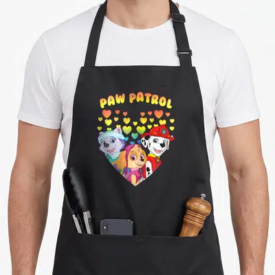 Funny patrol happy apron - PAW PATROL text over hearts and three puppies in yellow red blue pink — shown on a black cotton canvas apron against a white background