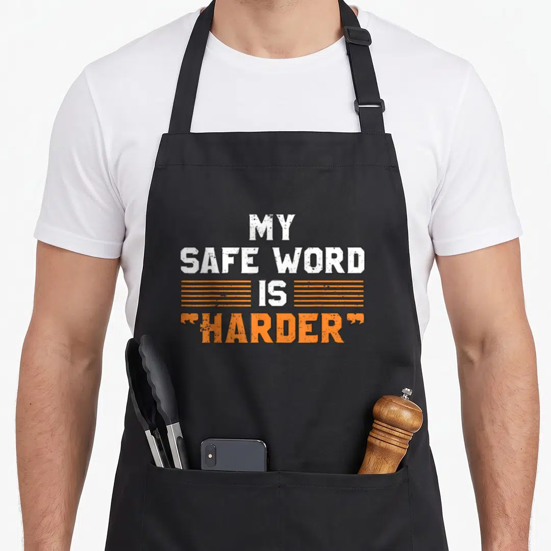 Safe the dirty apron - Stacked white and orange text reading MY SAFE WORD IS HARDER with horizontal lines — shown on a black cotton canvas apron against a white background