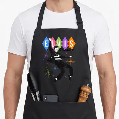 Elvis star apron - Dancing Elvis Presley graphic with five colorful diamonds and starbursts on gray background — shown on a black cotton canvas apron against a white background