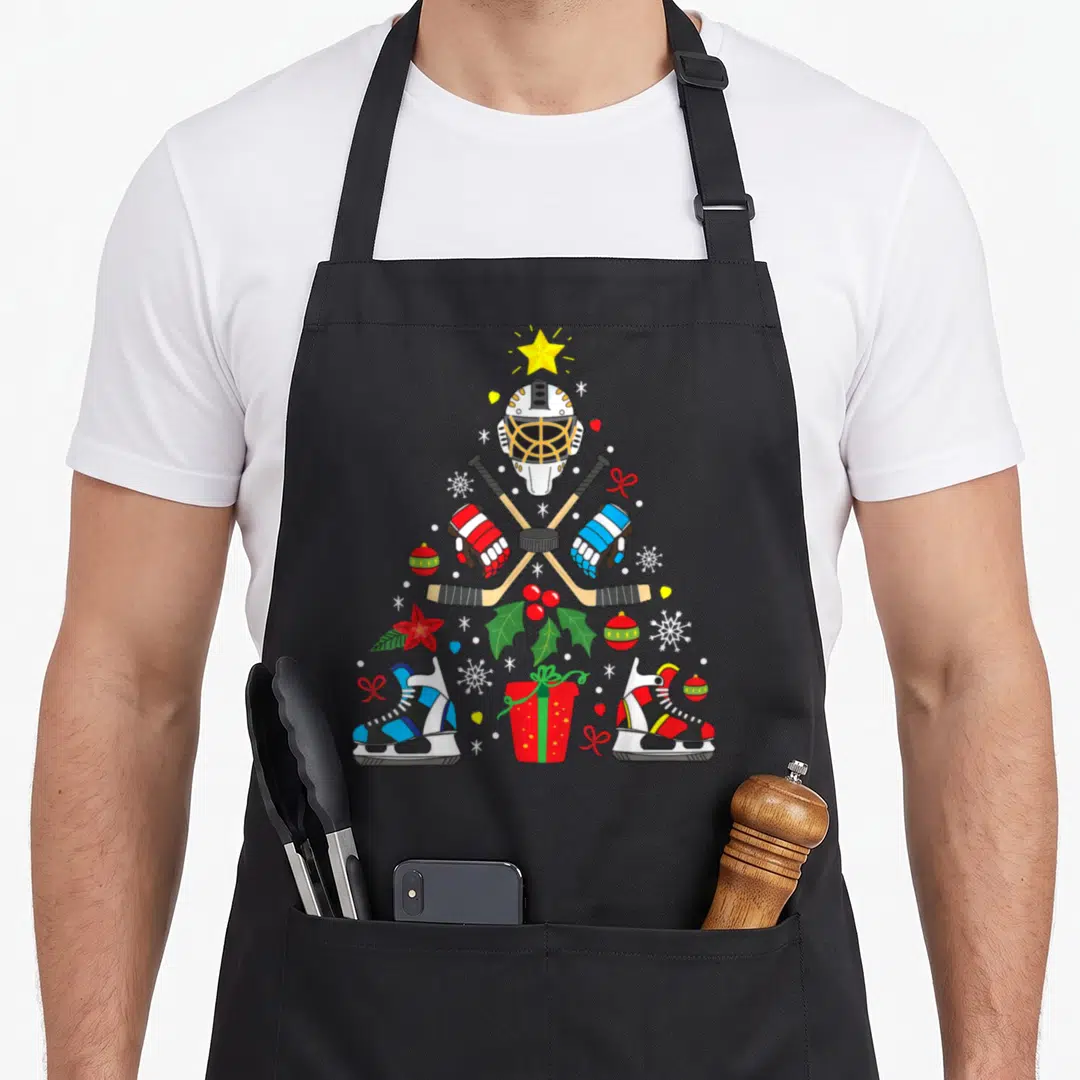 Ice christmas tree apron - Hockey helmet, skates, sticks, and ornaments arranged in a Christmas tree shape — shown on a black cotton canvas apron against a white background
