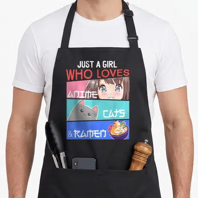 Otaku cat apron - Just A Girl Who Loves Anime Cats Ramen text with cartoon girl cat and noodle bowl in pink cyan blue — shown on a black cotton canvas apron against a white background
