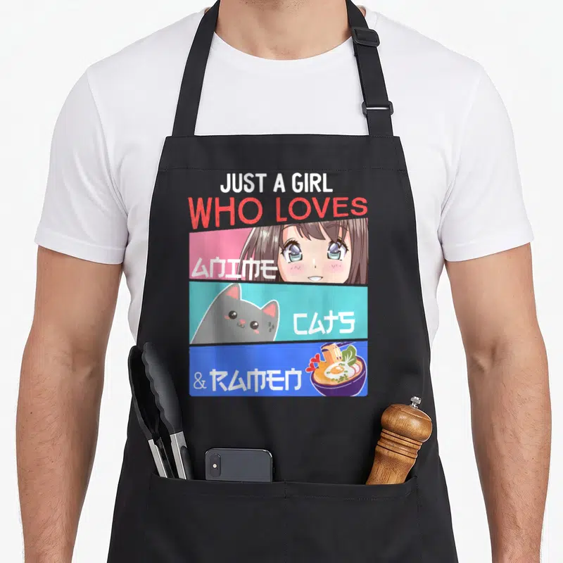 Otaku cat apron - Just A Girl Who Loves Anime Cats Ramen text with cartoon girl cat and noodle bowl in pink cyan blue — shown on a black cotton canvas apron against a white background
