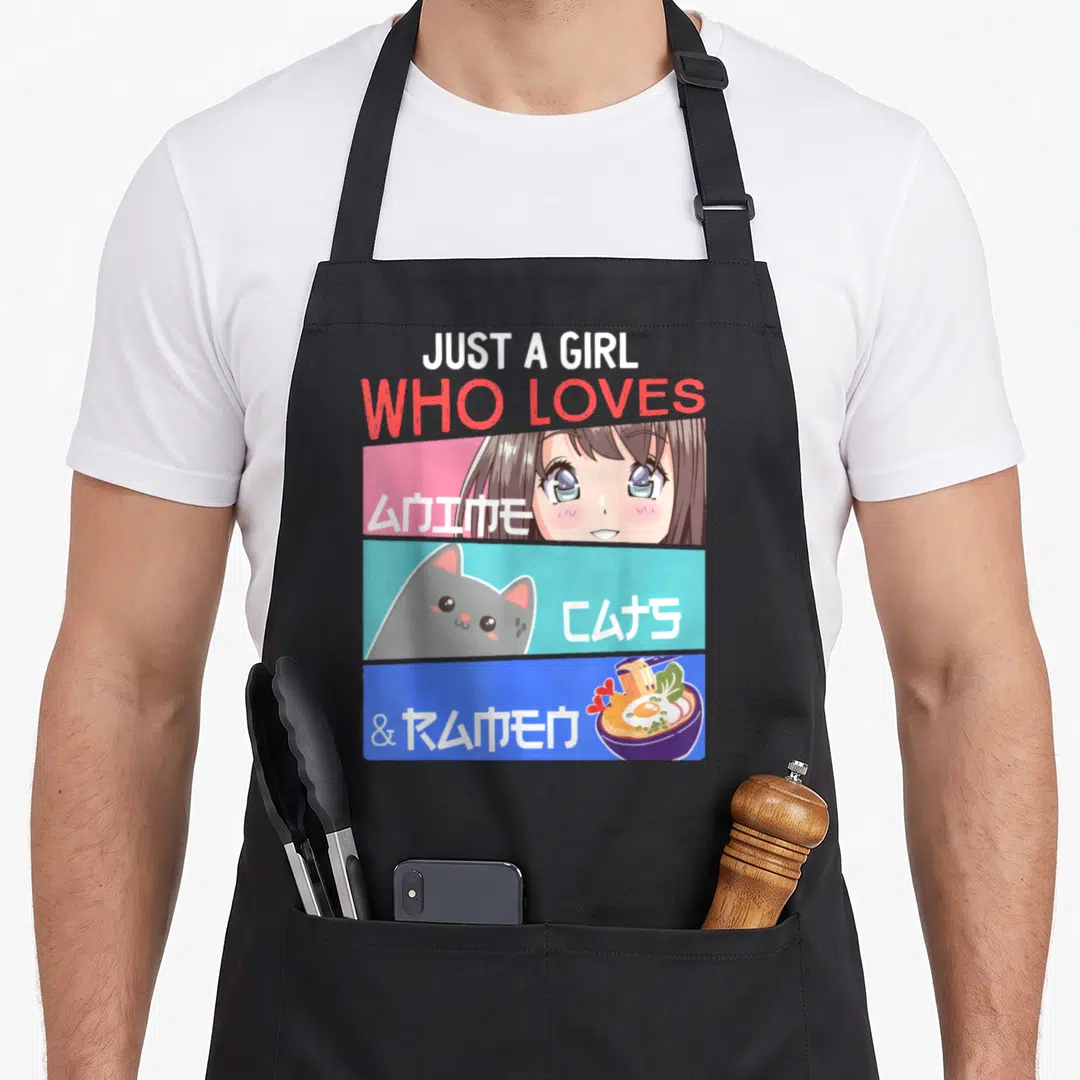 Otaku cat apron - Just A Girl Who Loves Anime Cats Ramen text with cartoon girl cat and noodle bowl in pink cyan blue — shown on a black cotton canvas apron against a white background