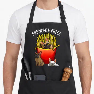 Retro frenchie french bulldog apron - FRENCHIE FRIES text above red fry box with three cartoon dogs in brown, white — shown on a black cotton canvas apron against a white background
