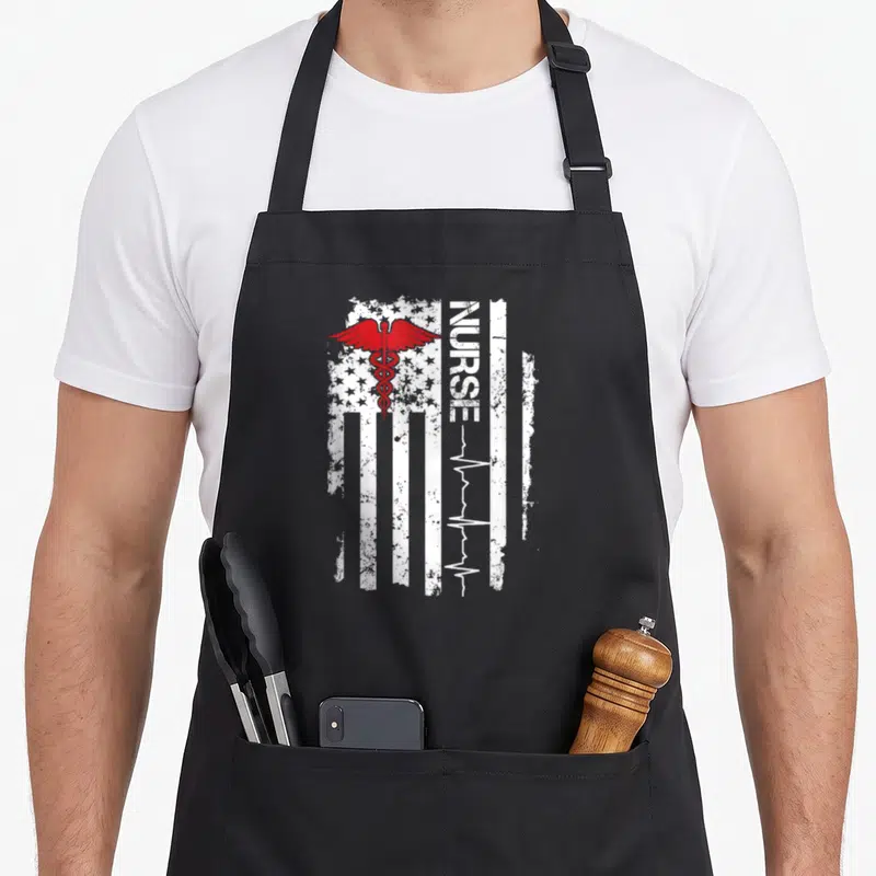 Pulse nurse apron - Distressed white flag with red caduceus and vertical NURSE text ending in heartbeat line — shown on a black cotton canvas apron against a white background