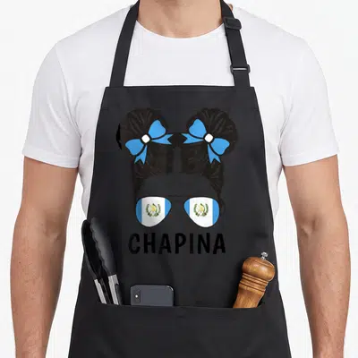 Chapina guatemalan aprons - Woman's hair in two buns with blue bows, sunglasses reflecting Guatemalan flag, CHAPINA — shown on a black cotton canvas apron against a white background
