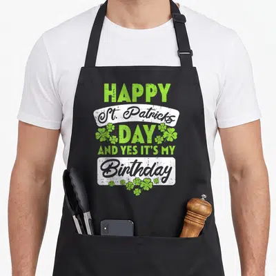Birthday irish aprons - HAPPY St Patricks DAY AND YES IT'S MY Birthday text with green shamrocks and white banners — shown on a black cotton canvas apron against a white background