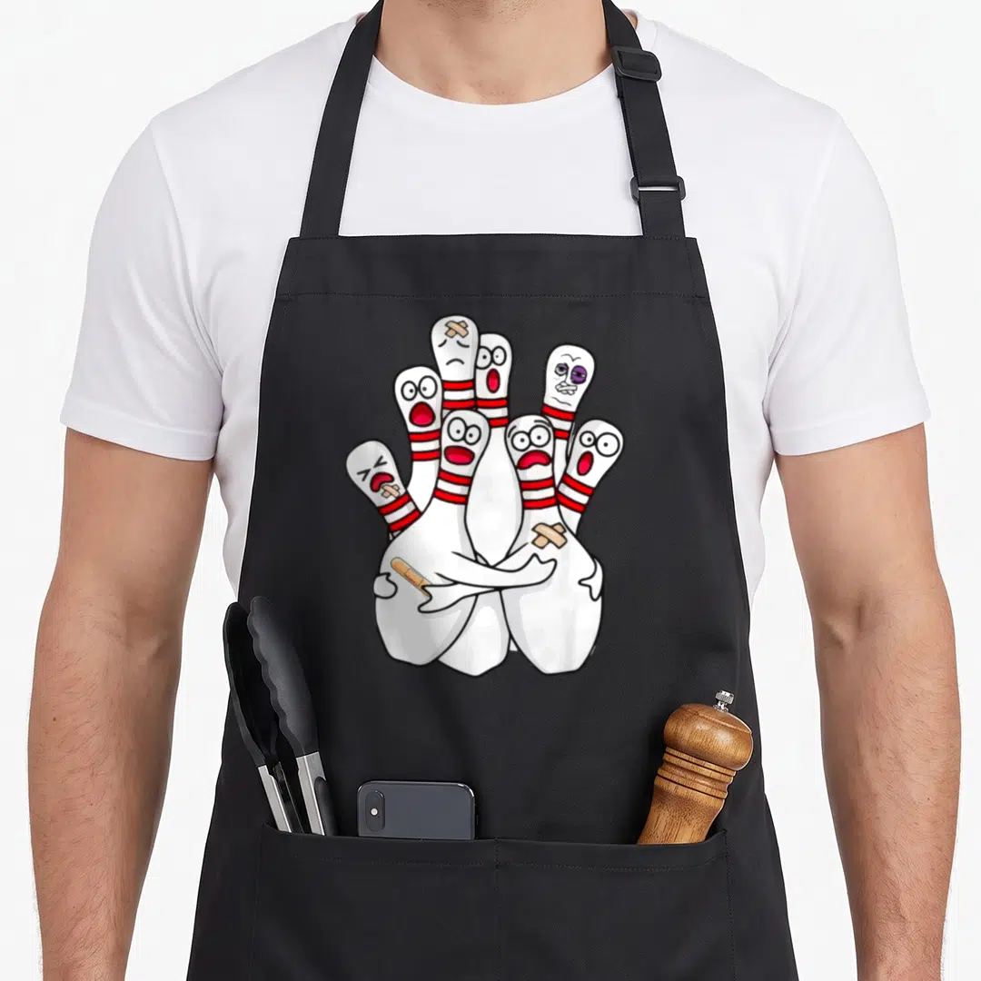 Bowling cartoon apron - Cartoon white bowling pins with red stripes huddling together wearing beige bandages on heads — shown on a black cotton canvas apron against a white background