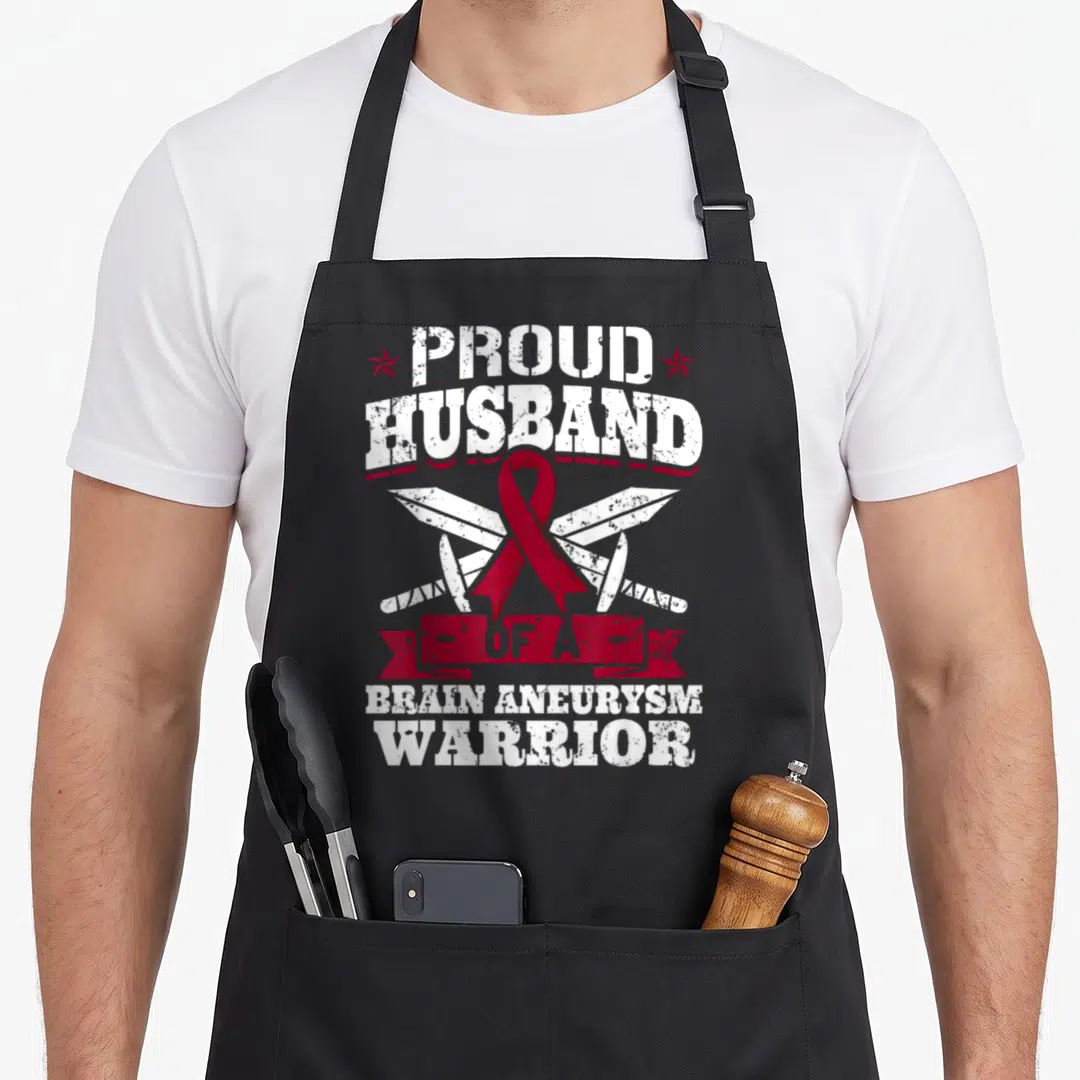 Proud husband apron - Red ribbon over crossed swords with Proud Husband Brain Aneurysm Warrior text — shown on a black cotton canvas apron against a white background