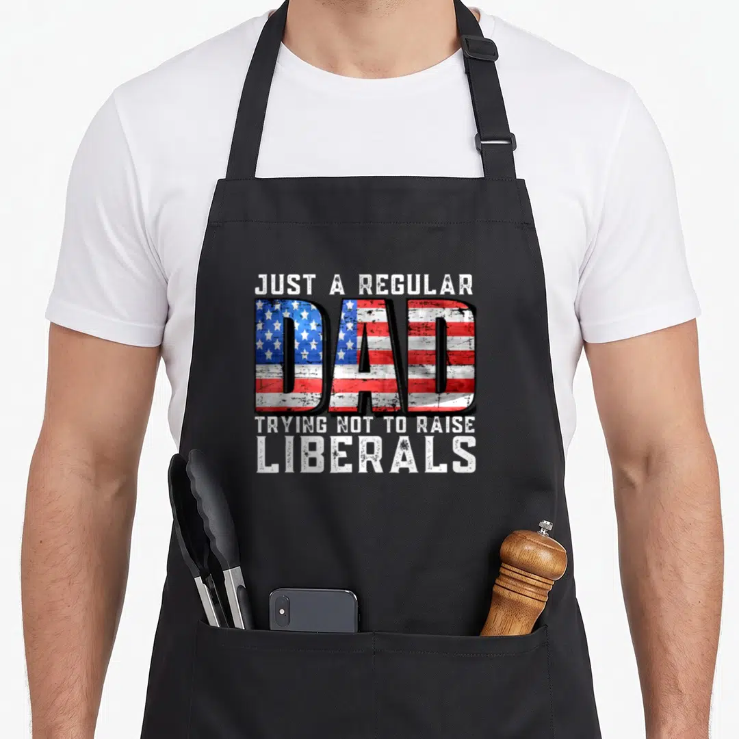 Trying dad apron - Distressed text design with American flag pattern filling the word DAD among white lettering — shown on a black cotton canvas apron against a white background