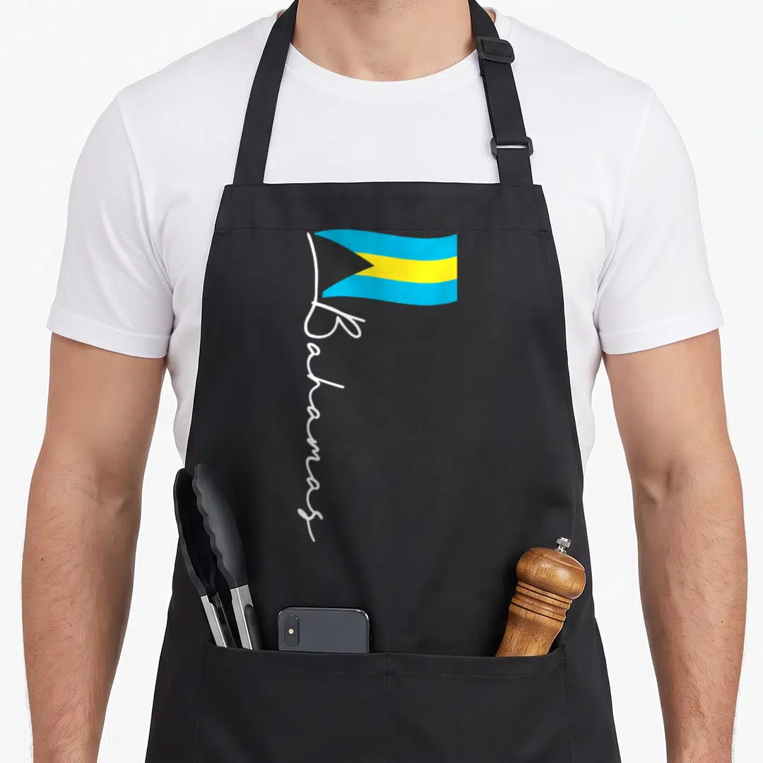 Bahamas pride apron - Bahamas flag with vertical white script below in blue, yellow, black, and white — shown on a black cotton canvas apron against a white background